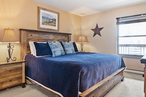 A bedroom with a wooden bed frame, a blue quilted bedspread, and two bedside tables with lamps.