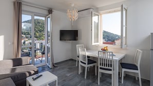 Ein modernes Wohnzimmer mit Essbereich, einem an der Wand befestigten Fernseher und Blick auf einen Hügelhang.