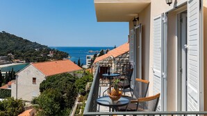 Ein Balkon mit Meerblick, Gartenmöbel und ein Steinhaus im Hintergrund.