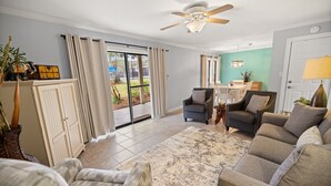 Ein geräumiges Wohnzimmer mit einer großen Couch, zwei Sesseln, einem Couchtisch und einem Deckenventilator. Eine Glast ür öffnet sich zu einem Patio.