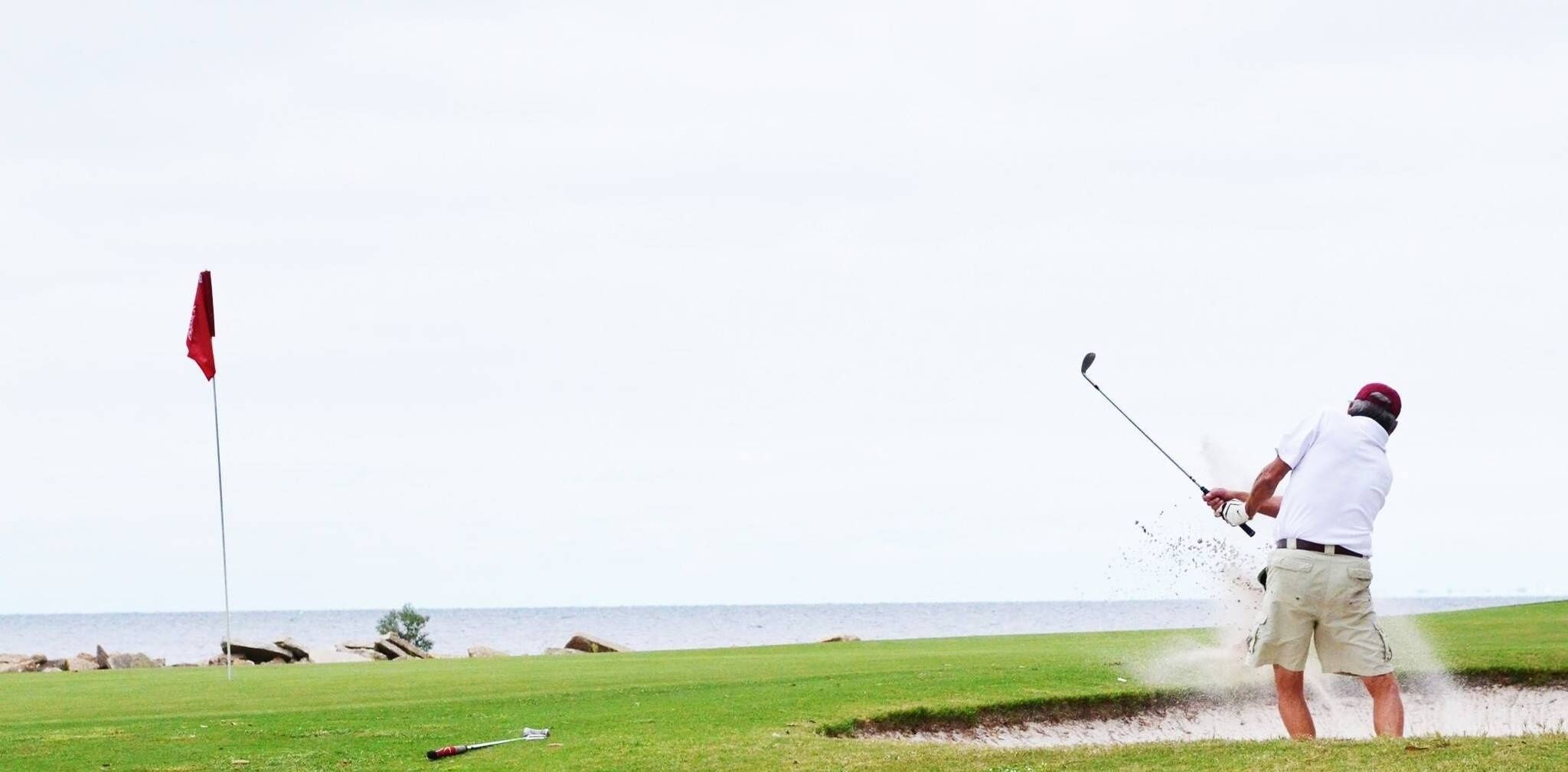 A man playing golf on a course with a flag in the distance.