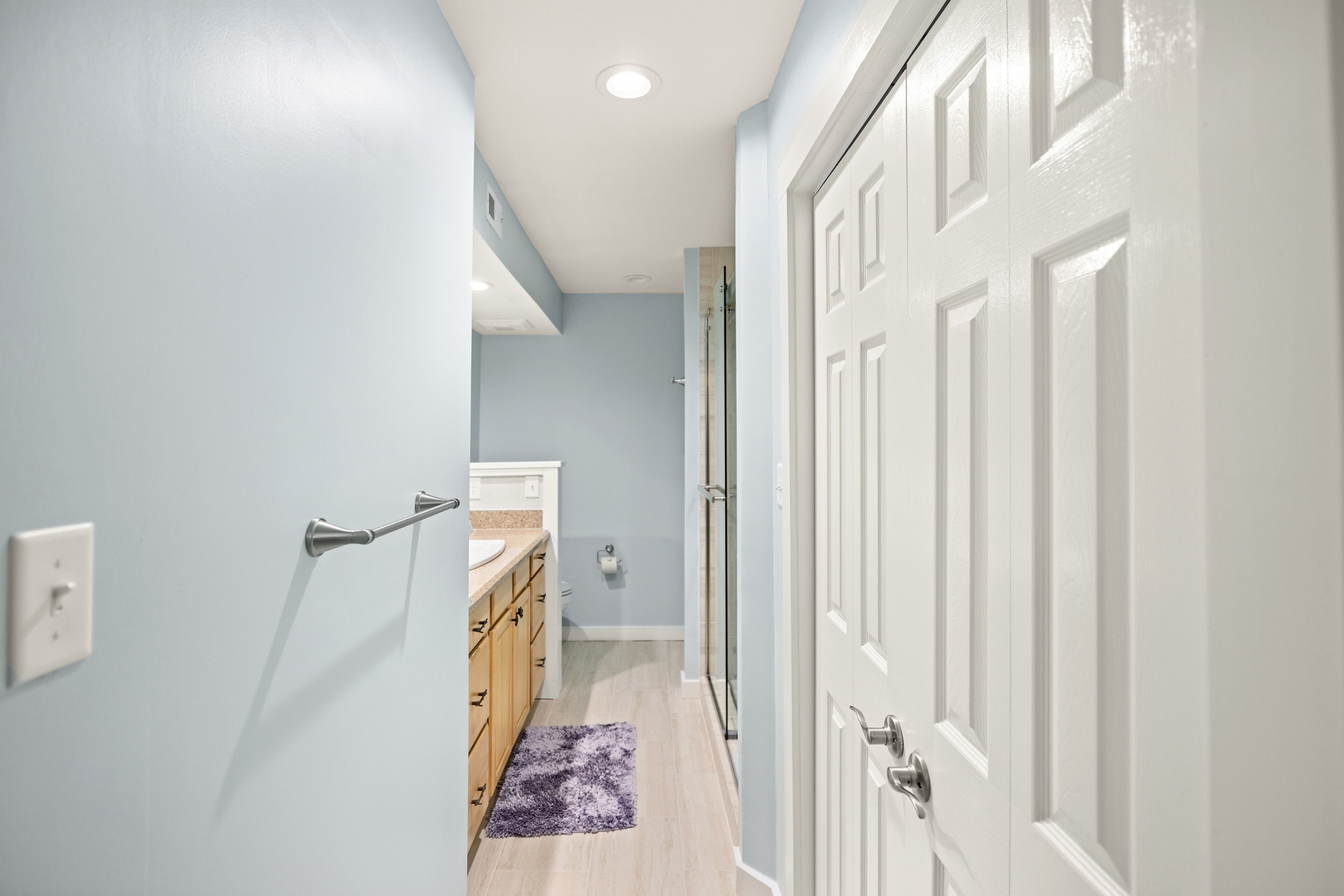 A hallway with a light blue wall, a white door, and a wooden cabinet with a countertop.