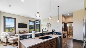 A modern kitchen with a large island, wooden cabinets, and pendant lighting. - The Cottage at Heritage Hill (Sugarcreek)