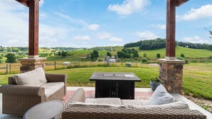 A covered outdoor seating area with wicker furniture and a stone pillar, overlooking a green landscape. - The Cottage at Heritage Hill (Sugarcreek)
