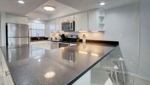 A modern kitchen with white cabinets, a stainless steel refrigerator, a microwave, and a granite countertop. - 346 El Matador 2 Bedroom Home by RedAwning (Fort Walton Beach)