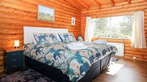 A wooden cabin bedroom with a bed, a nightstand, a window with curtains, and a picture on the wall. - Rocksite (Blairgowrie)