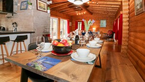 A wooden cabin with a long dining table set for a meal, a kitchen area, and a cozy living space with a fireplace. - Rocksite (Blairgowrie)