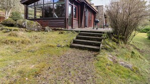 A log cabin with a glass extension, stone steps, and a patio area. - Rocksite (Blairgowrie)