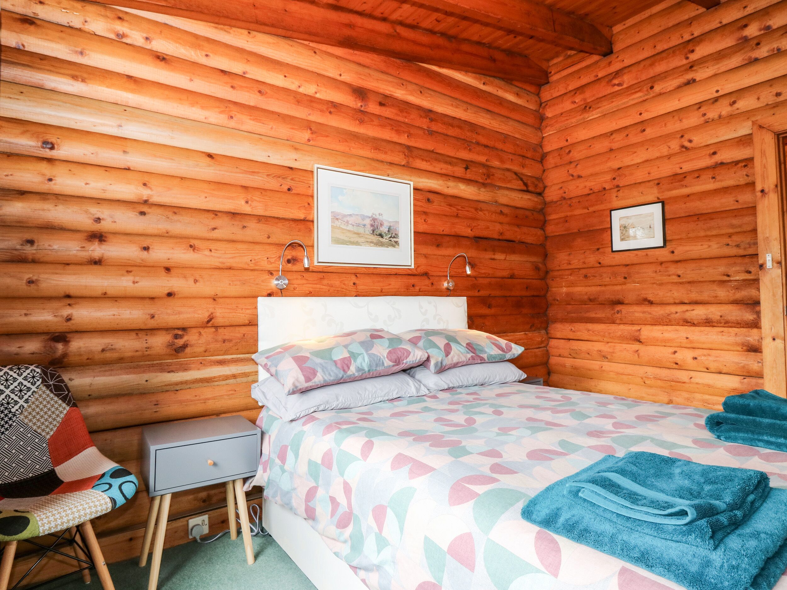 A cozy wooden cabin bedroom with a bed, pillows, a nightstand, and a chair.