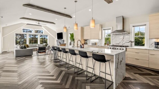Une cuisine moderne dotée d’un îlot central, de tabourets de bar et d’un parquet en bois disposé en chevrons.