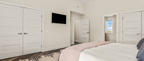 Ein Schlafzimmer mit einem großen Bett, weißen Wänden, einem Deckenventilator und einem an der Wand montierten Fernseher.
