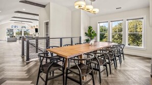 Un vaste espace dédié à la salle à manger, avec une longue table en bois, des chaises noires et un luminaire suspendu.
