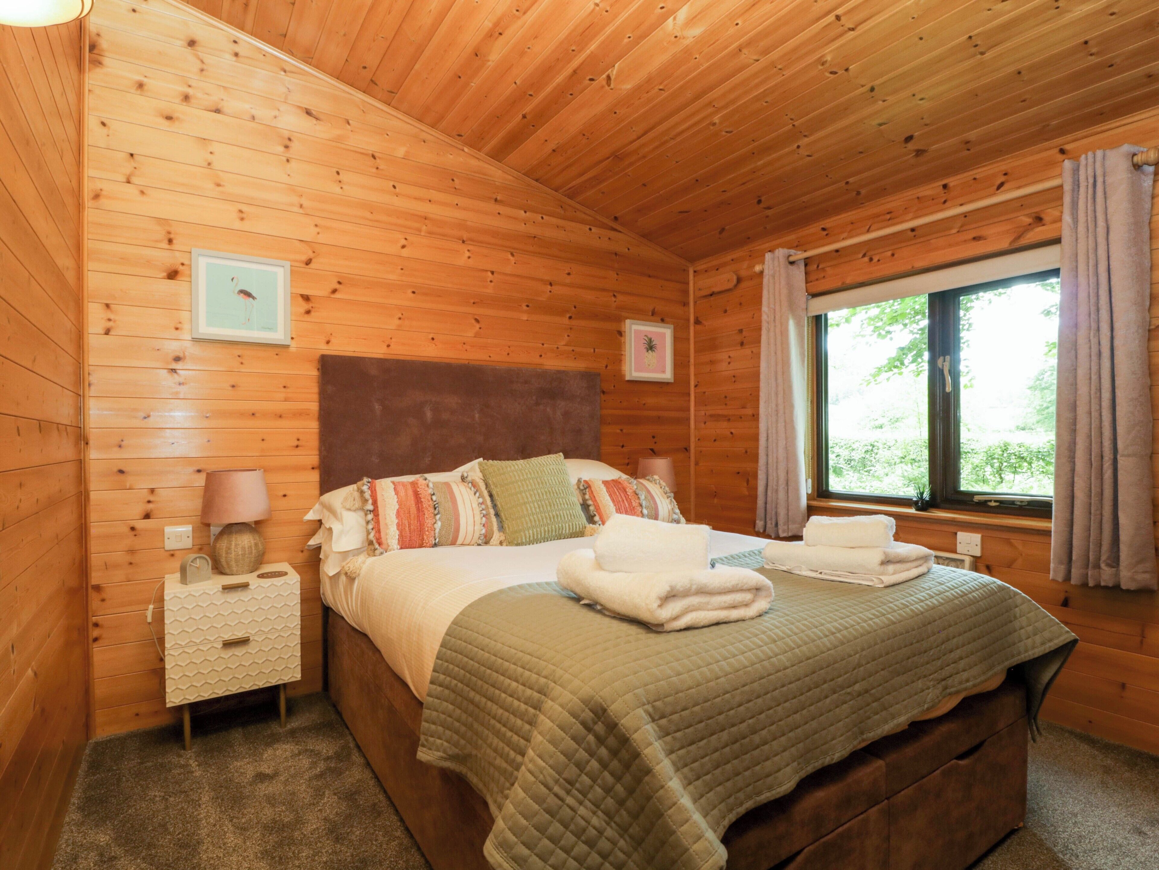 Een houten slaapkamer met een bed, nachtkastjes, een raam met gordijnen en een aan de wand bevestigd schilderij.