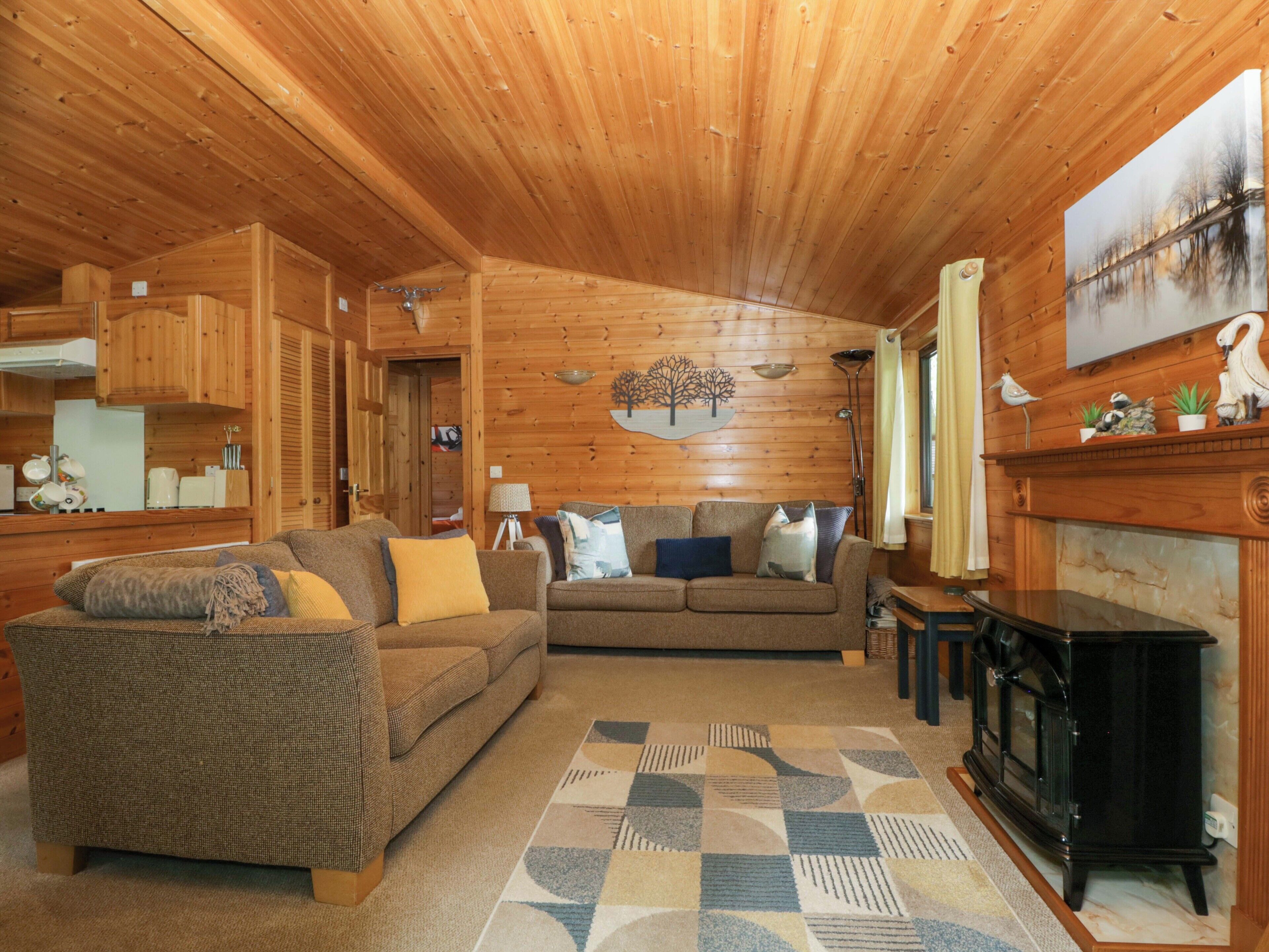 Een houten chalet van binnen met een bank, een kamerkleed met dessin, een open haard en een eethoek.
