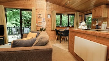 Een gezellig chaletinterieur met een eethoek, een keuken met een bar en grote ramen met uitzicht op de natuur.