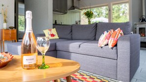 Un soggiorno moderno con un divano grigio, un tavolino in legno, una bottiglia di vino e un bicchiere.
