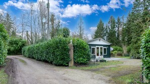 Una strada di campagna che conduce a una piccola casa a un solo piano con tetto verde, immersa nel verde e circondata da alberi alti.