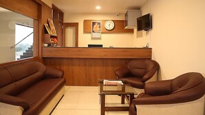 Uma área de recepção com um balcão de madeira, um relógio e uma televisão. Há dois sofás de couro castanho e uma mesa de centro de vidro.