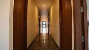Um corredor comprido e estreito, com portas de madeira em ambos os lados e chão brilhante e espelhado.