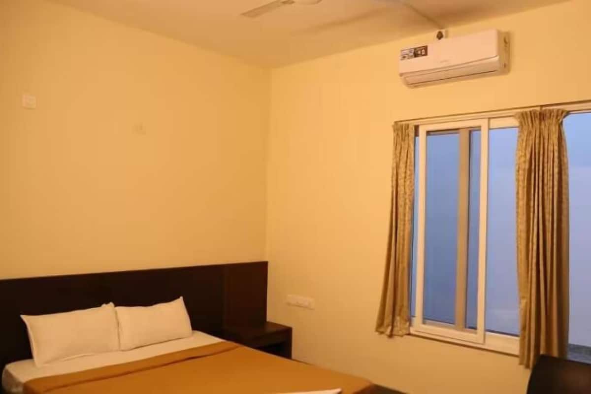 A hotel room with a bed, a nightstand, an air conditioner, and a window with curtains.