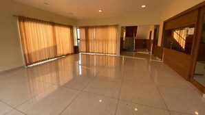Um quarto amplo com piso de azulejos, grandes janelas com cortinas, uma escada e uma porta de madeira.