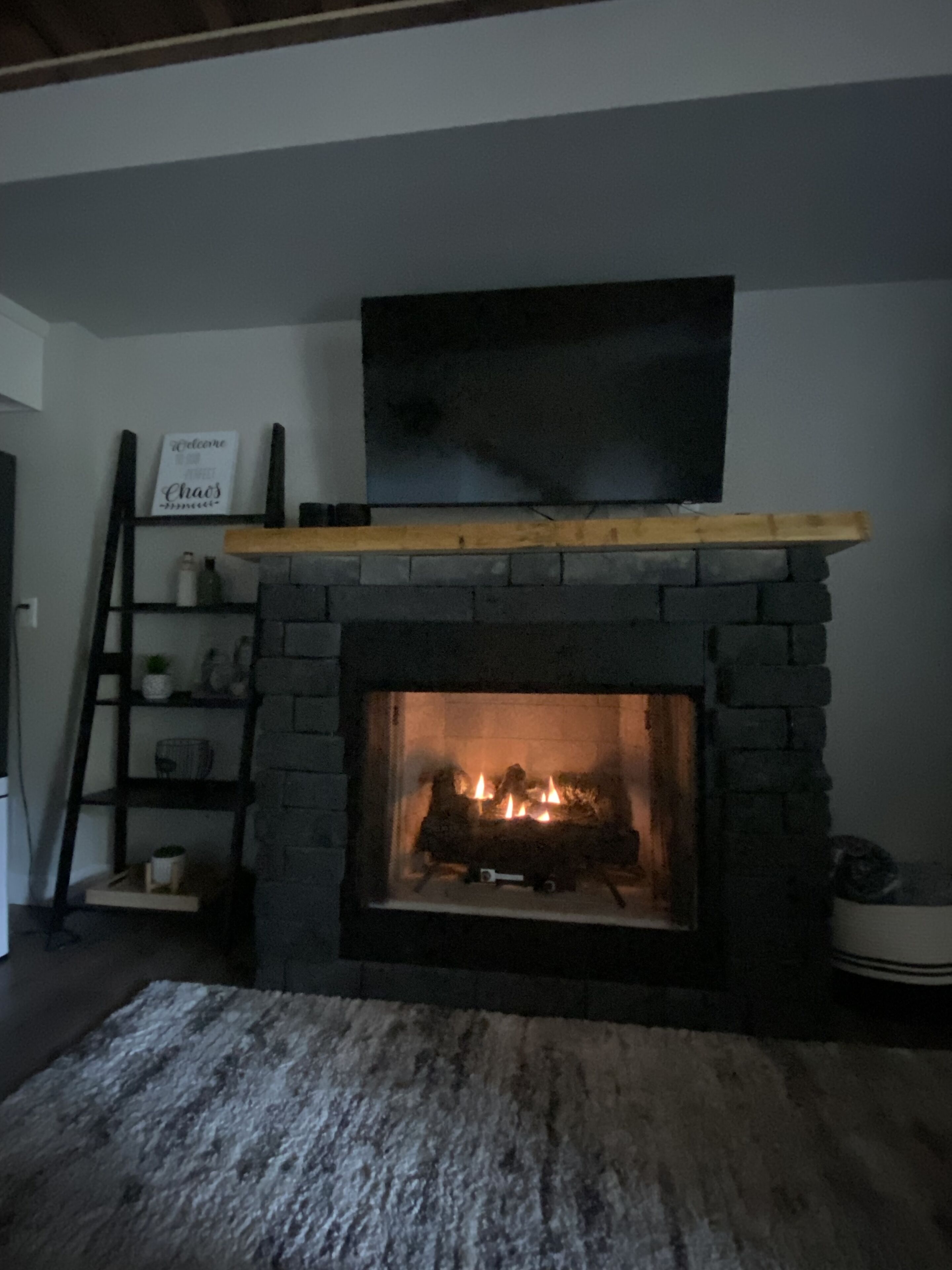Ein Steinkamin mit darüber montiertem Fernseher, ein Holzregal und eine Leiter zur Linke.