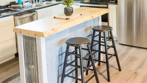Una cocina moderna con armarios blancos, techo de madera, refrigerador de acero inoxidable e isla central con taburetes.
