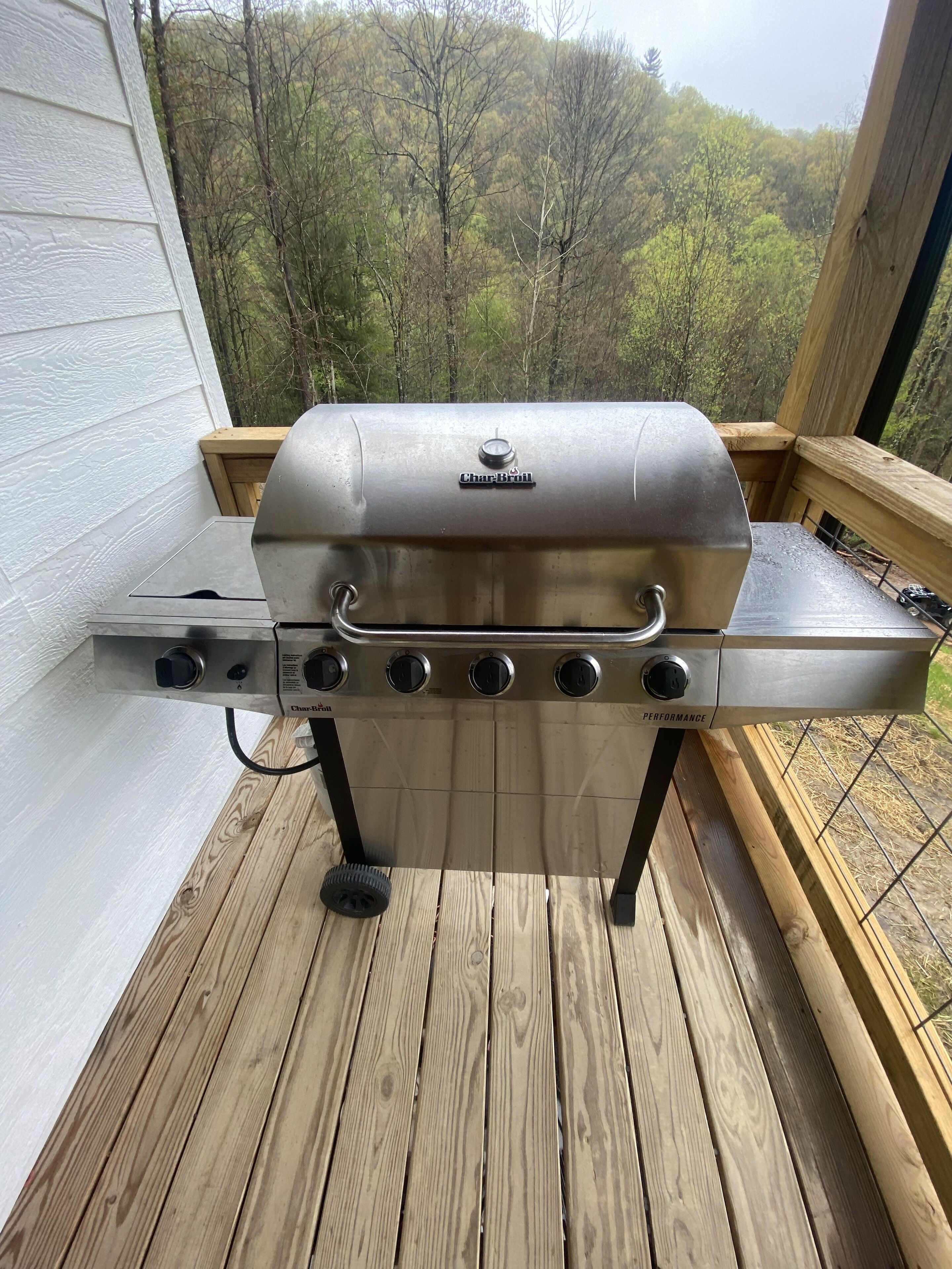 A Char-Broil gas grill on a wooden deck with a view of trees in the background.