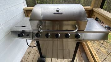 A Char-Broil gas grill on a wooden deck with a view of trees in the background.