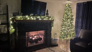 Una sala de estar acogedora con chimenea, un árbol de Navidad y un sillón cómodo.