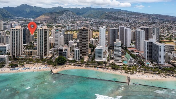 Un paisaje urbano costero con edificios altos, una playa y montañas al fondo.