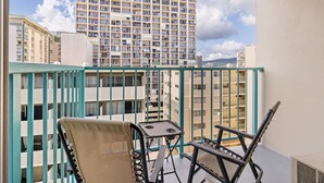 Un balcón con vista a un edificio alto, una silla y una mesita.