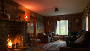 Ein gemütliches Wohnzimmer mit Kamin aus Stein, Holzwänden und einem großen Fenster mit Blick auf einen Garten.