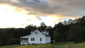 Ein weißes Haus mit einer Veranda, umgeben von einer grünen Wiese und dichter Baumgruppe.