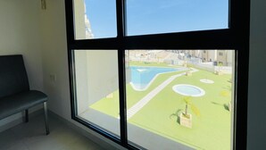 A room with a large window, a bench, and a view of a landscaped area with a pool. - 3090 RESIDENCIAL SABRINA (Orihuela Costa)