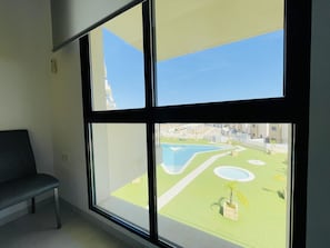 A room with a large window, a bench, and a view of a landscaped area with a pool.