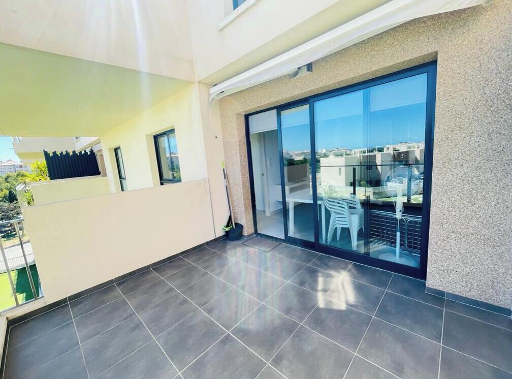 A modern interior with a tiled floor, a sliding glass door leading to a balcony, and a view of the cityscape.