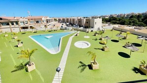 A pool area with a large pool, surrounded by green artificial grass, palm trees, and umbrellas. - 3090 RESIDENCIAL SABRINA (Orihuela Costa)