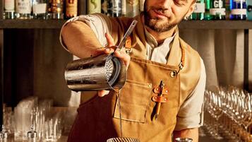 A bartender preparing a drink with a variety of bottles in the background.