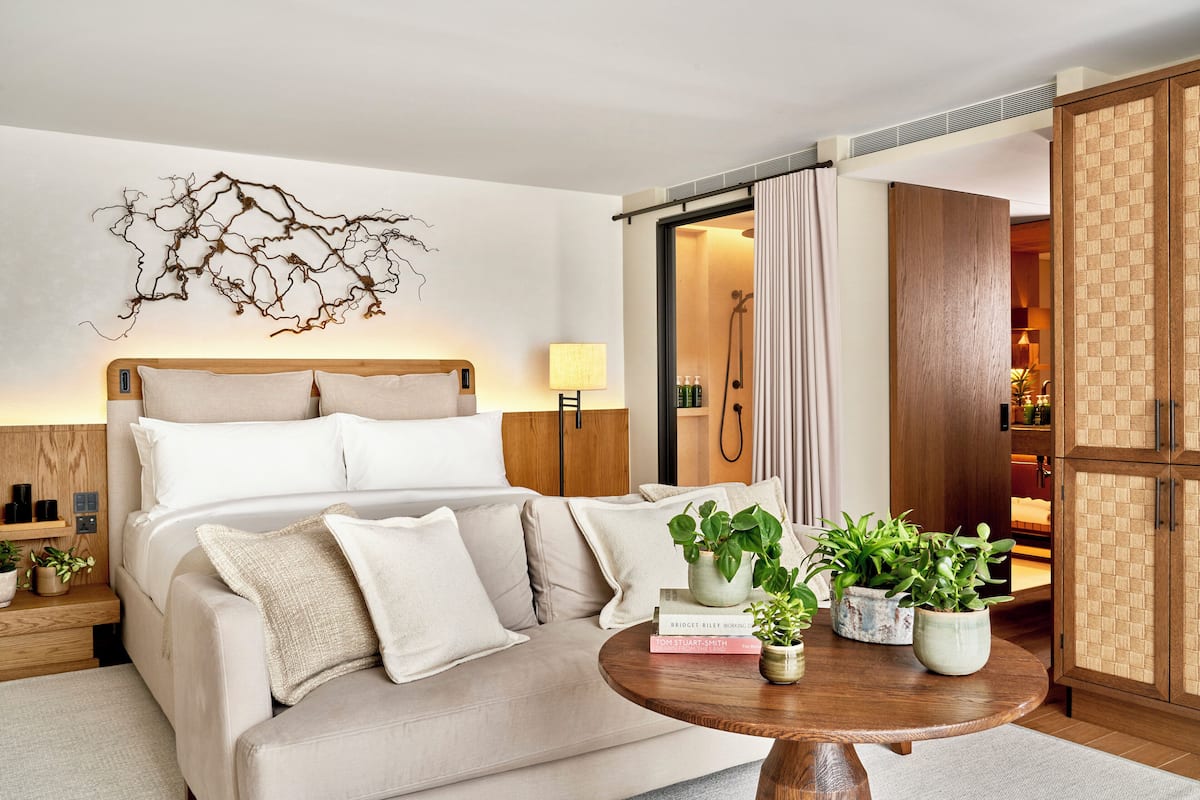 Quarto de hotel moderno com cama, mesa de cabeceira, abajur e vista para um banheiro.