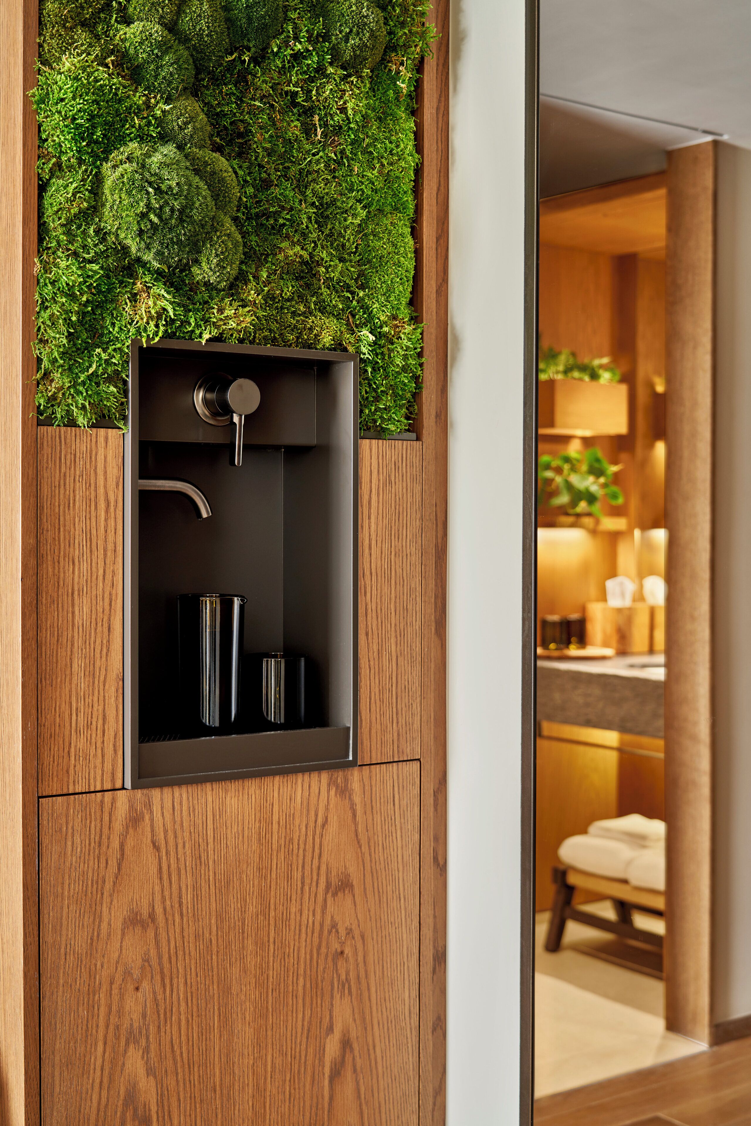 A modern bathroom with a built-in sink, wooden cabinetry, and a moss wall.