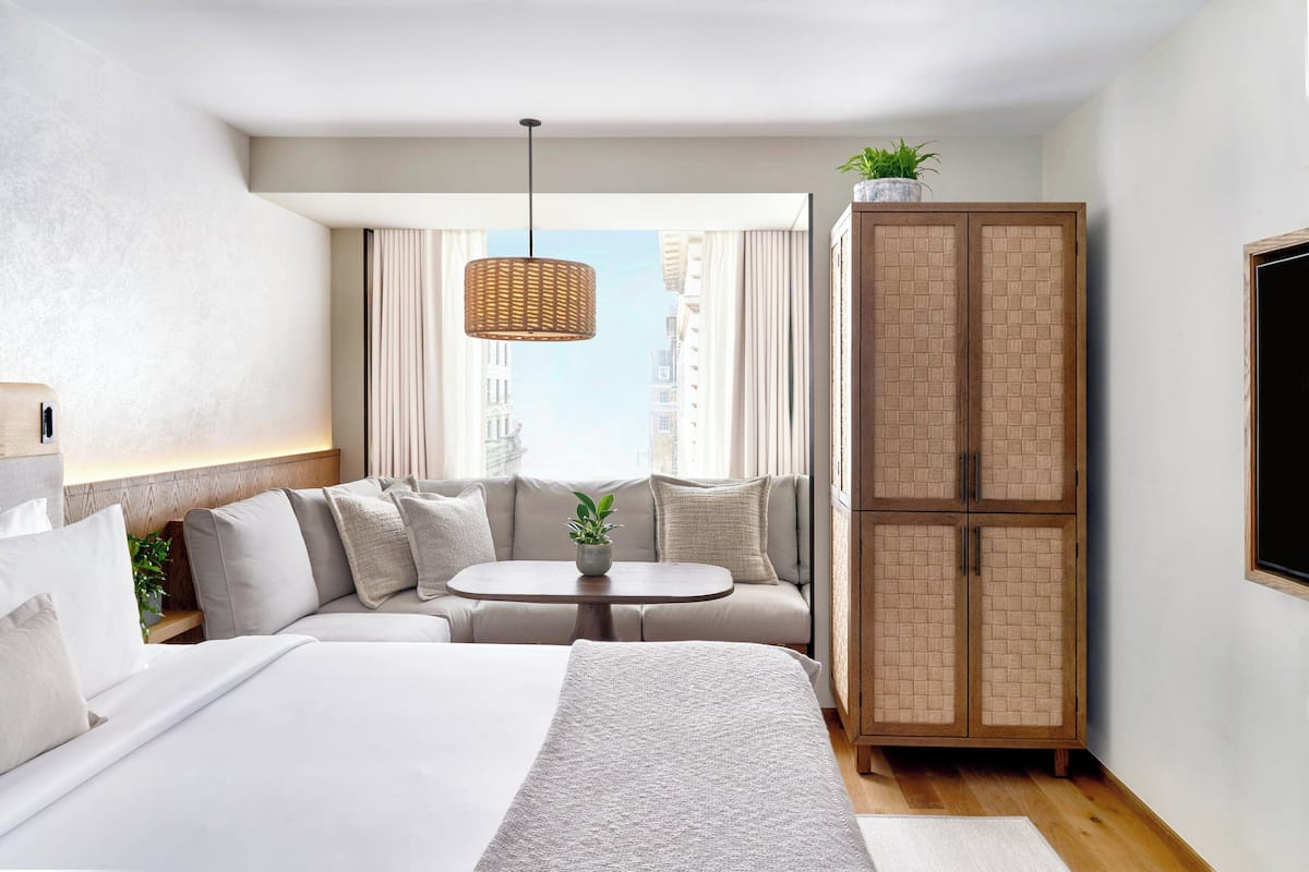 A modern hotel room with a large bed, a sofa, a small table, and a wardrobe.