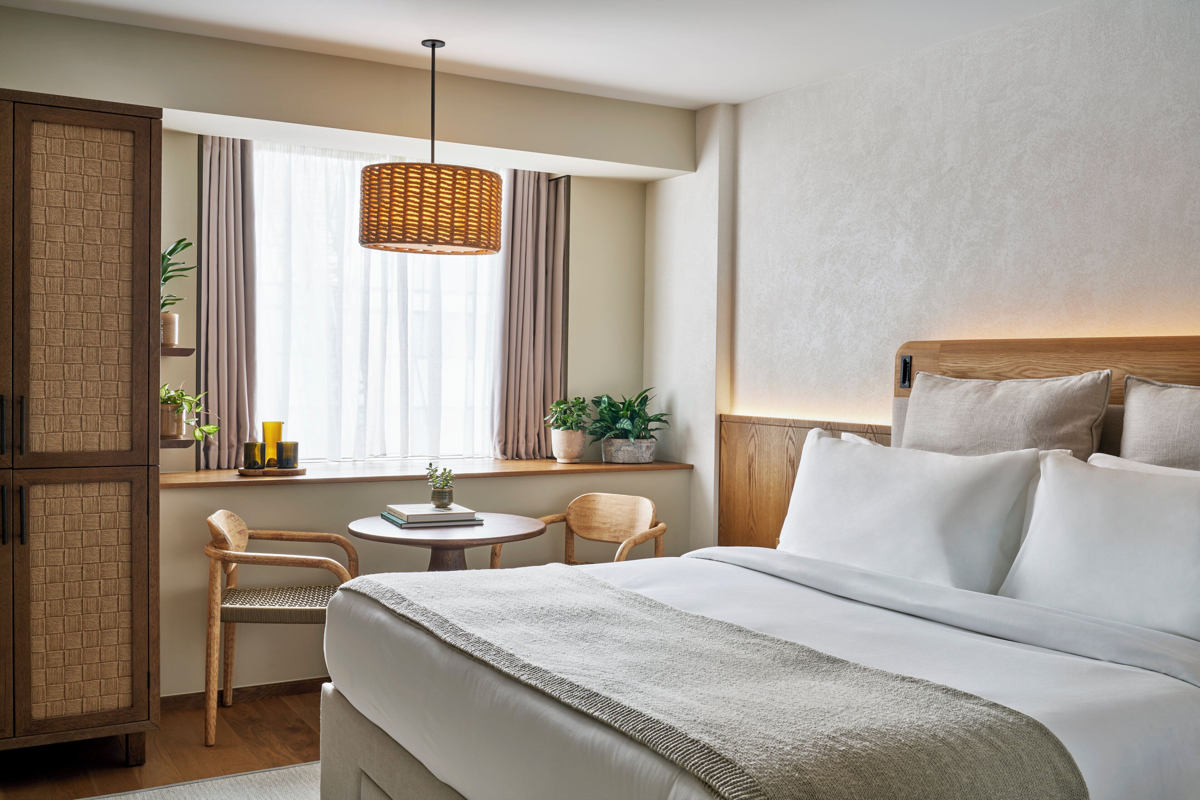 Ein Hotelzimmer mit einem Bett, einem kleinen Tisch, zwei Stühlen, einem Fenster mit Vorhängen und einer Pendelleuchte.