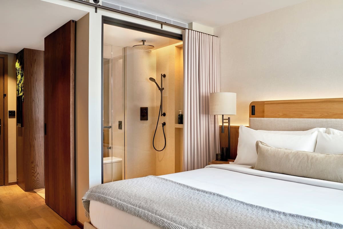 A modern hotel room with a large bed, a shower area, and a wooden wardrobe.