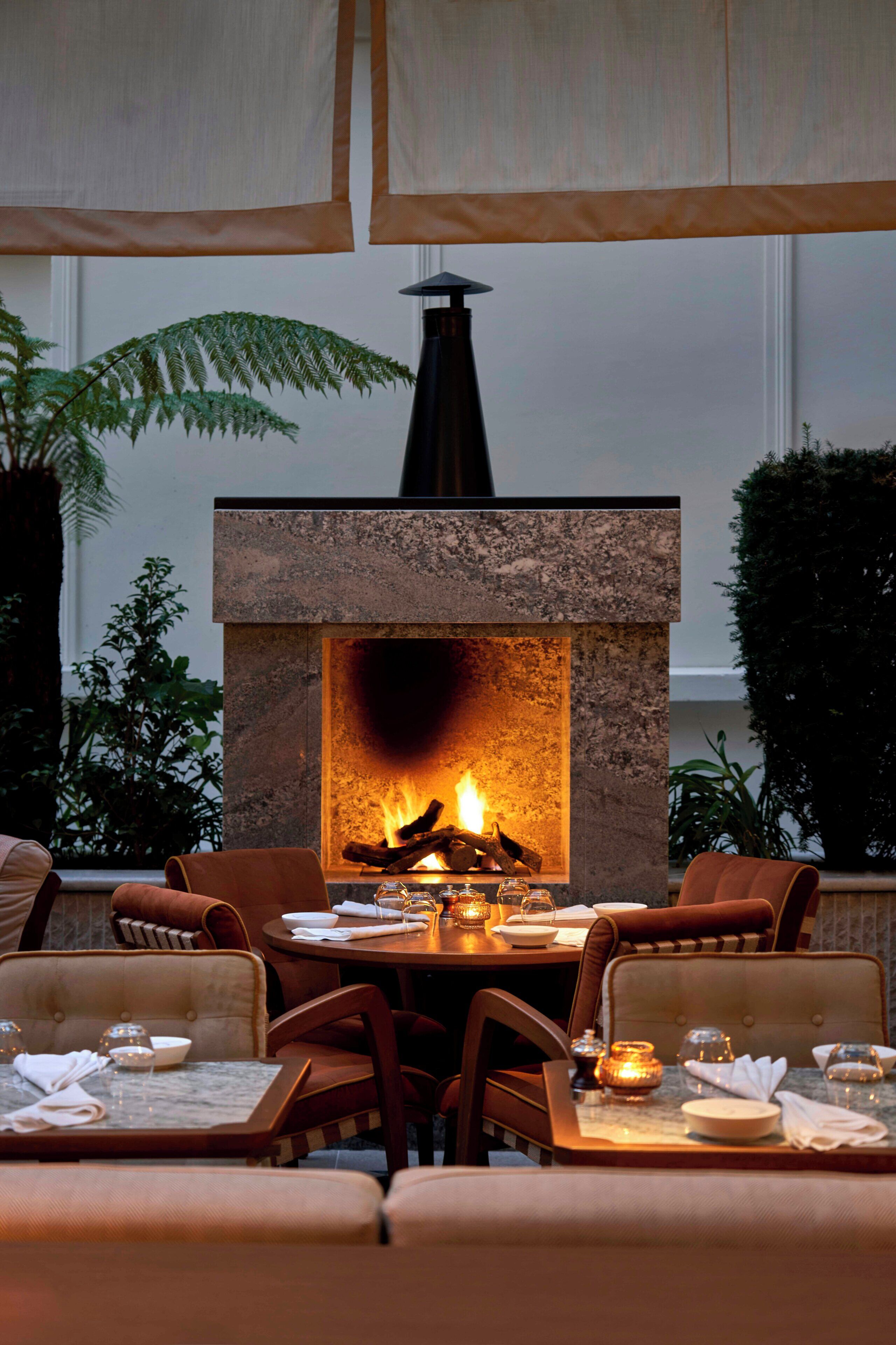 An outdoor dining area with a stone fireplace, seating, and potted plants.