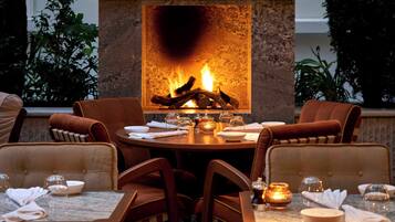An outdoor dining area with a stone fireplace, seating, and potted plants.