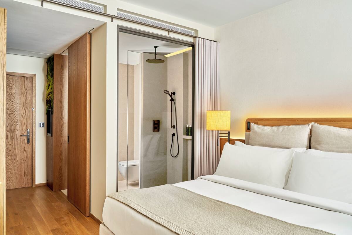 A hotel room with a bed, a shower, a wooden door, and a lamp.