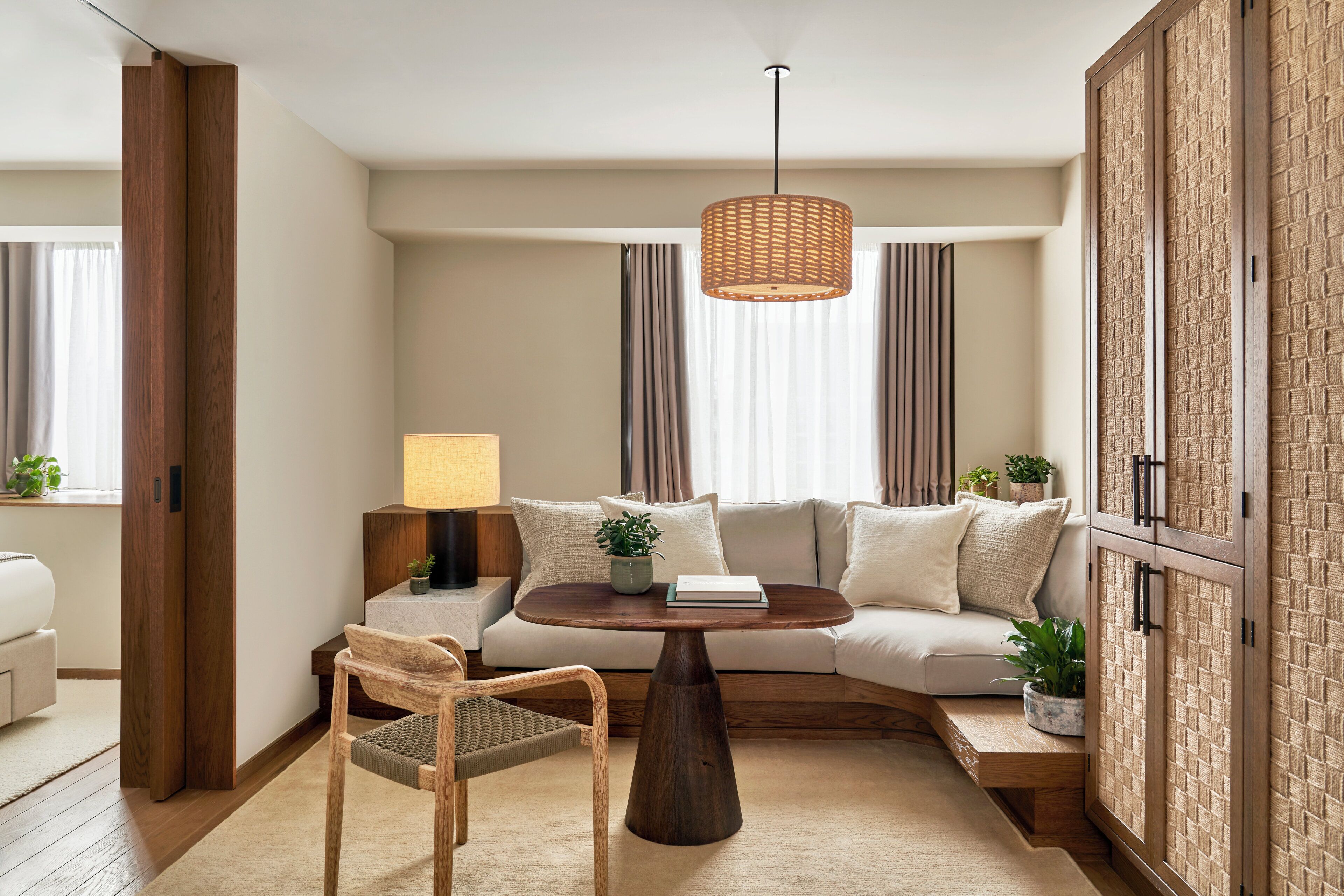 Un salon moderne comprenant un canapé, une table basse ronde en bois, un fauteuil en osier, un luminaire suspendu et un meuble en bois.
