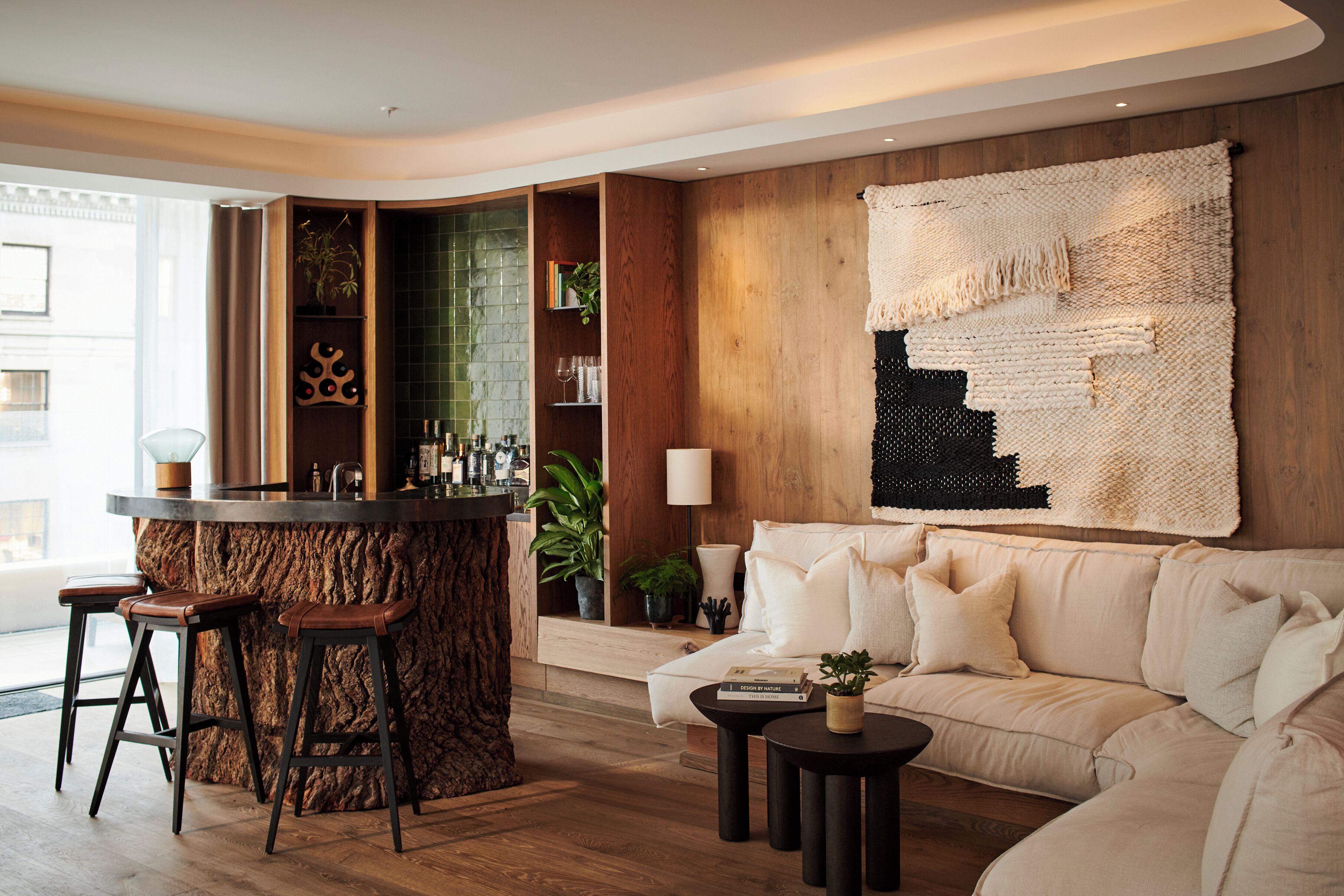 Un salon moderne doté d’un coin bar, d’une grande tapisserie tissée et d’un canapé agrémenté de coussins.