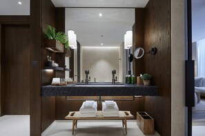 A modern bathroom with a large mirror, dual sinks, and a wooden bench with towels. - 1 Hotel Mayfair (London)